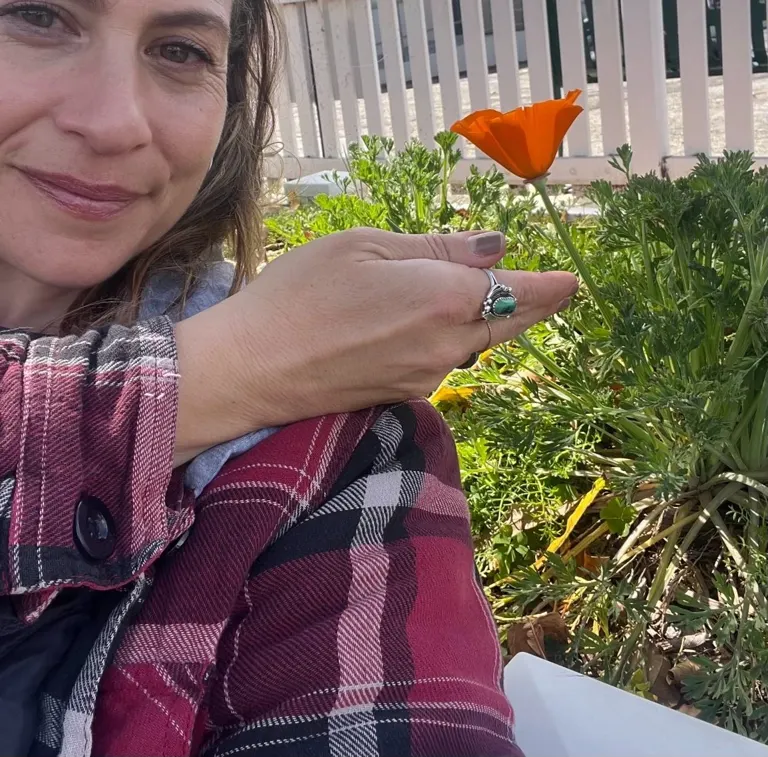 Mindy smiling beside a bright orange poppy in her kitchen garden